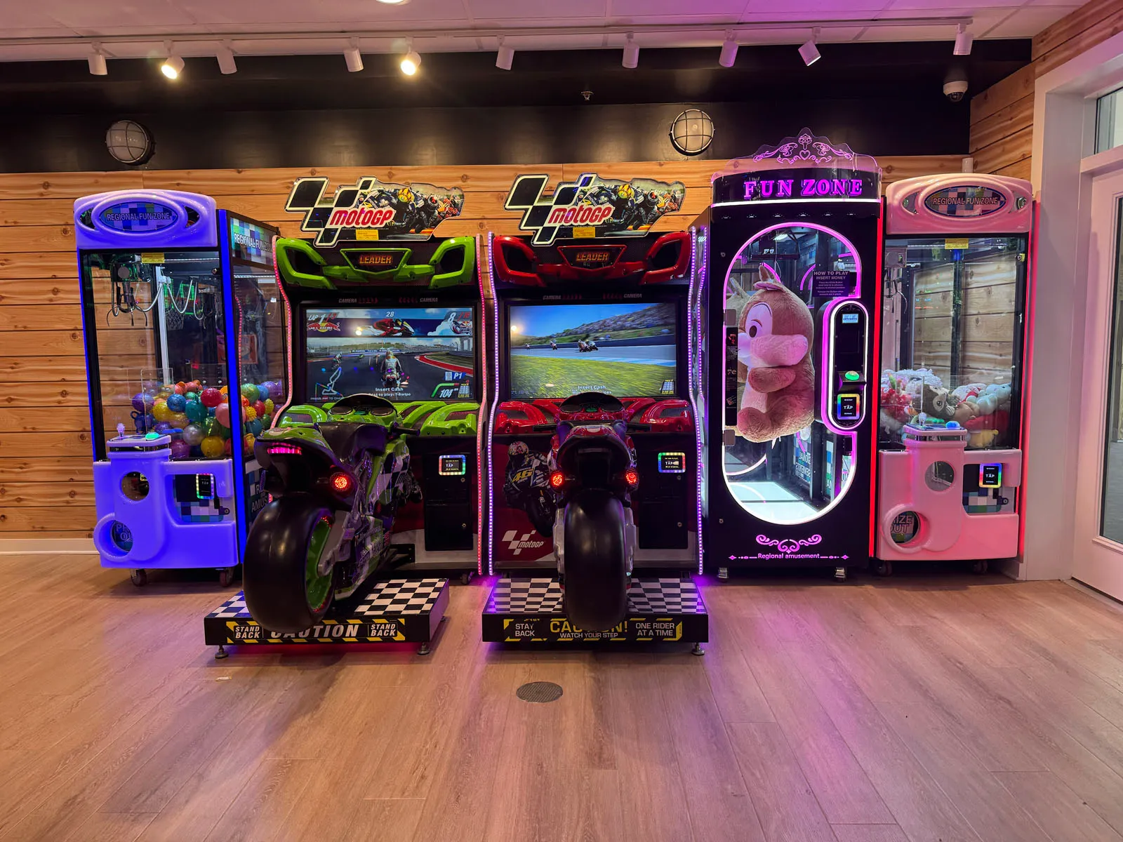 Two MotoGP racing games flanked by claw machines along a wood-plank wall