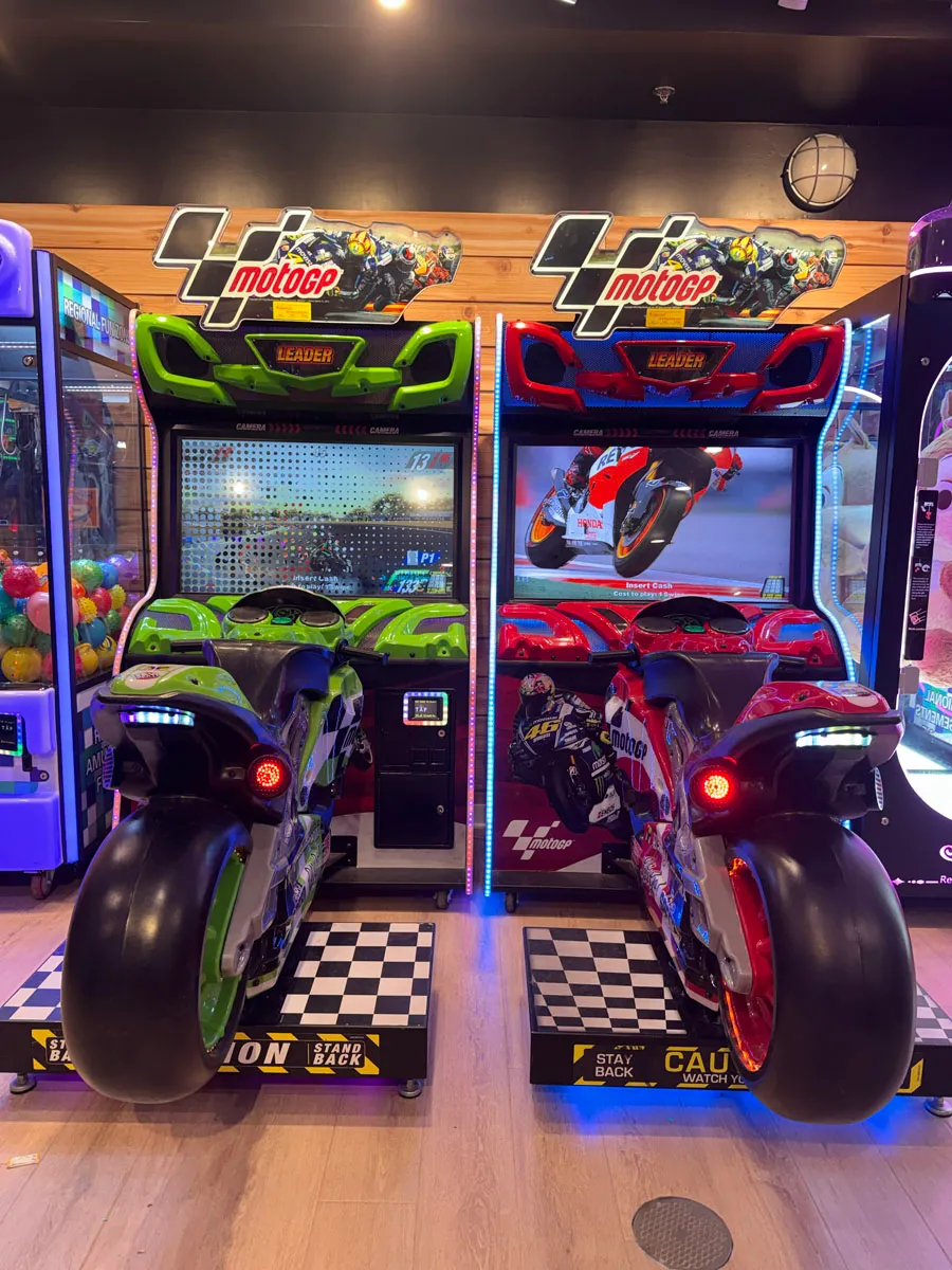 Two MotoGP motorcycle racing cabinets head-on with checkered floor mats
