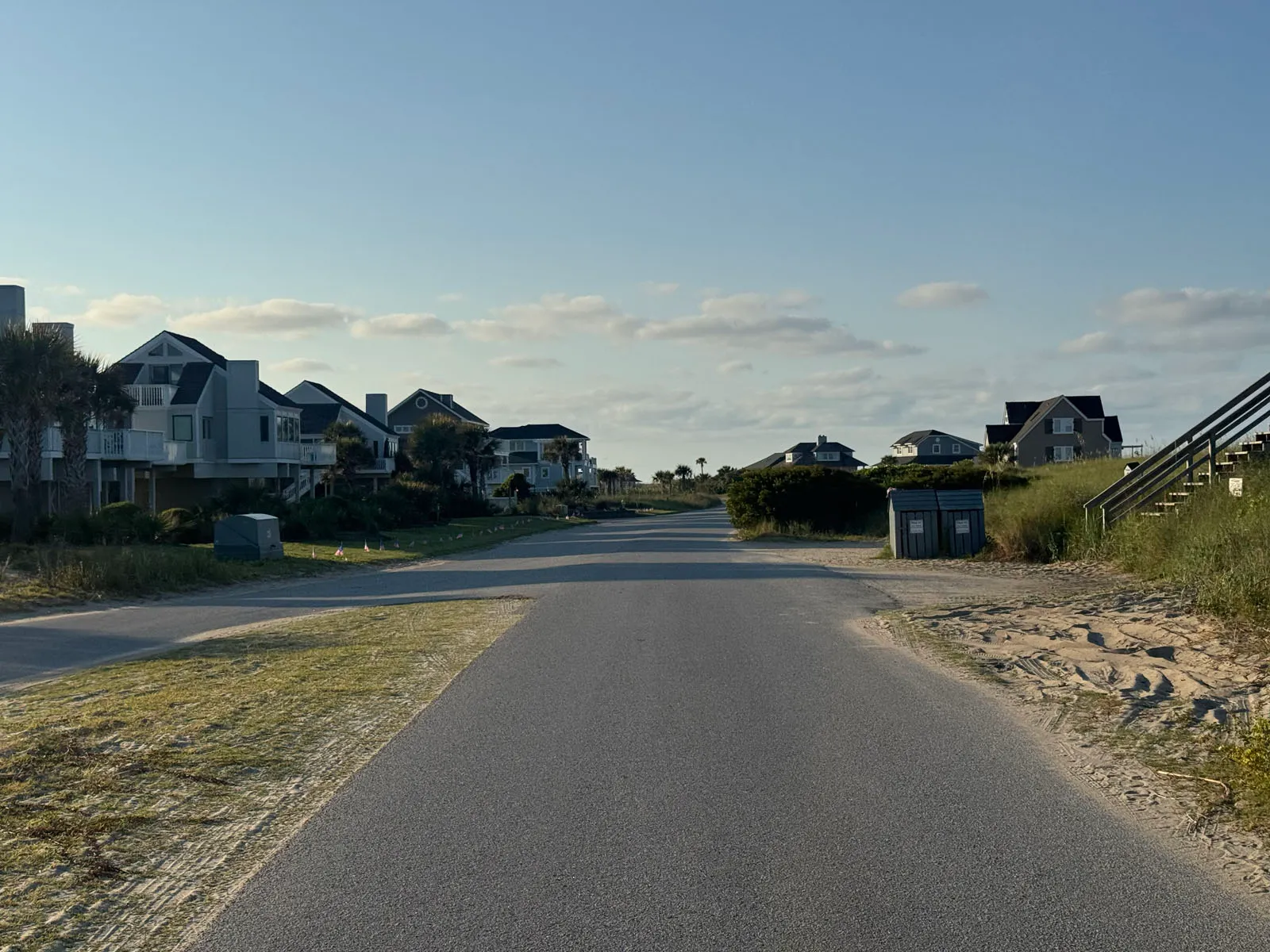 Beach access road toward dune crossover with homes lining street