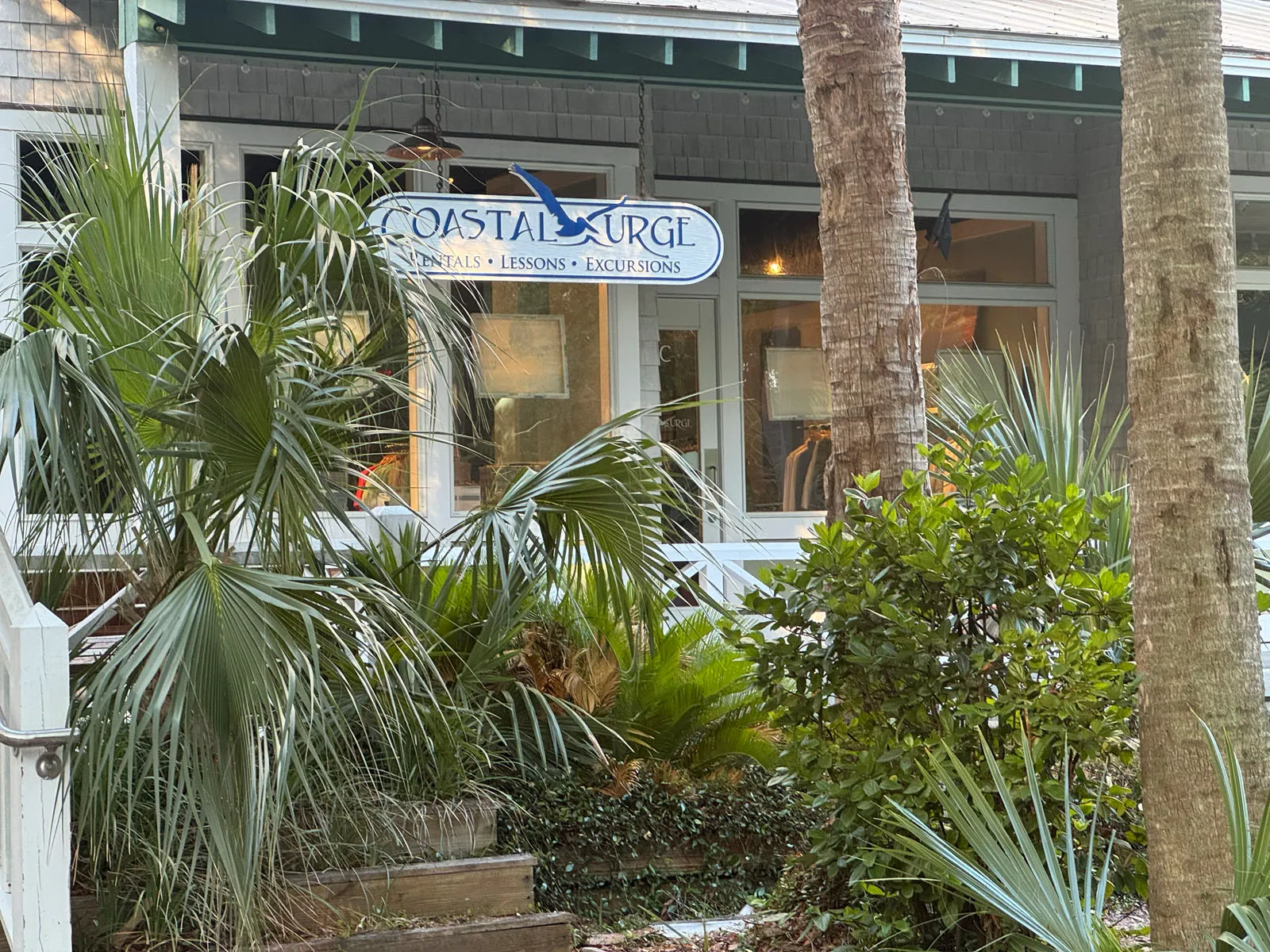 Coastal Urge shop sign among palms on porch