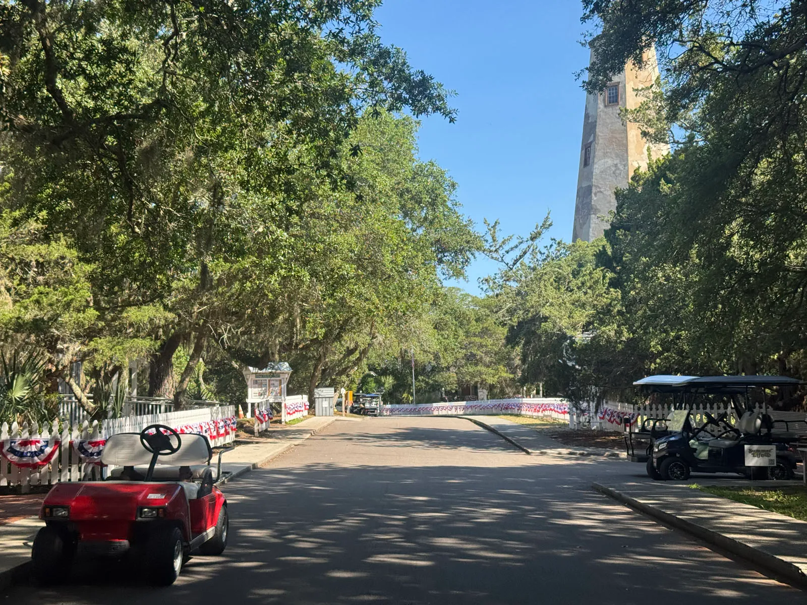 Red and other golf carts on shaded street near lighthouse
