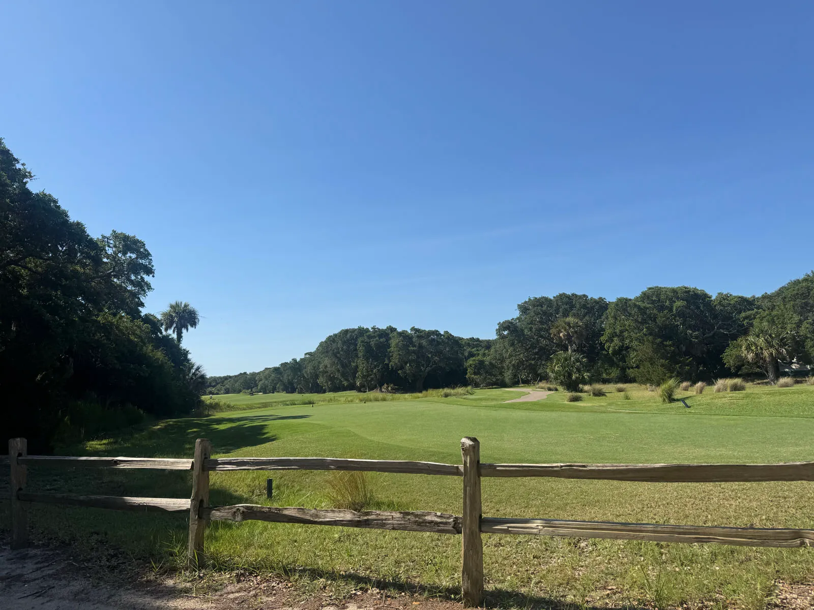 Expansive golf fairway and treeline under a clear sky