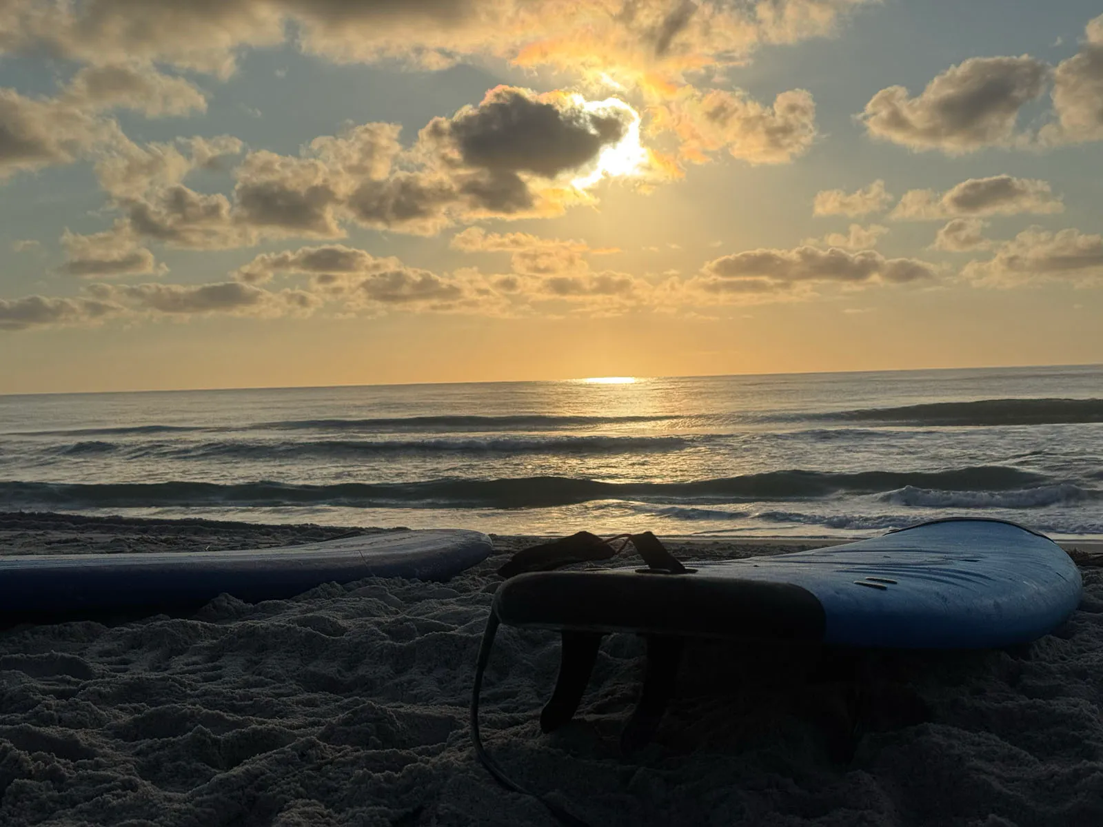Sunrise over ocean with surfboards on beach foreground