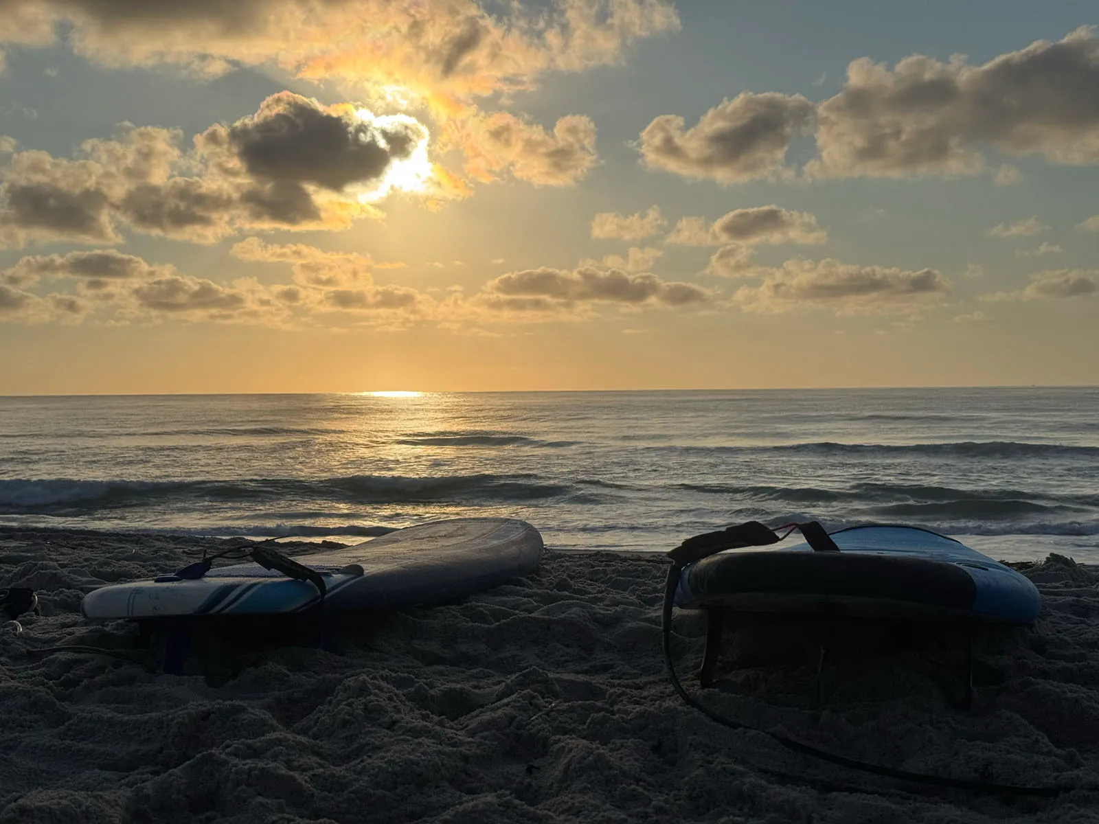 Sunrise over the surf with two surfboards laid on the sand