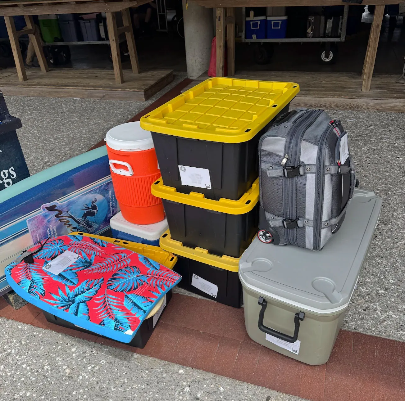 Coolers, black-and-yellow storage totes, and a rolling bag staged on the terminal floor with luggage tags