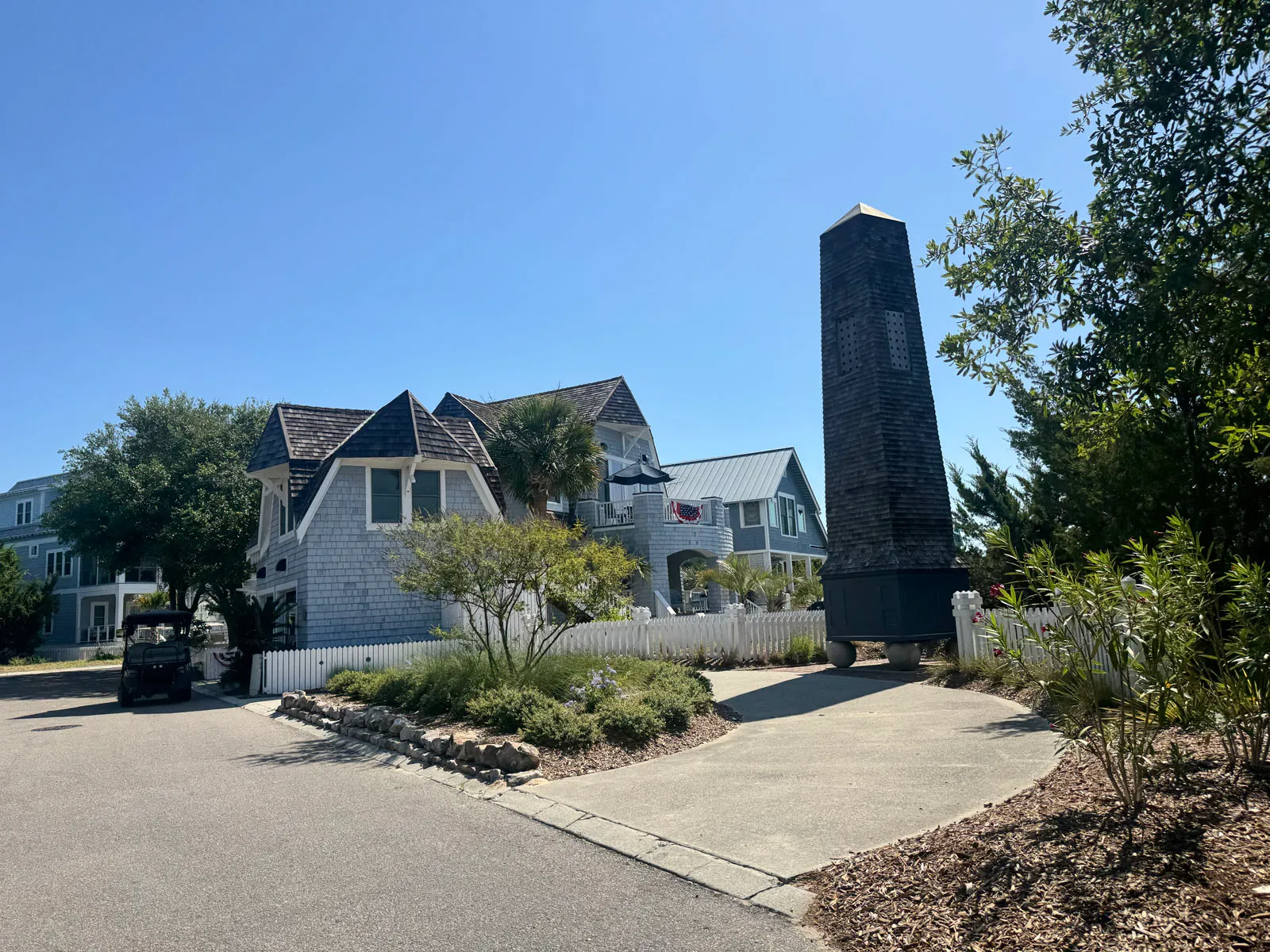 Shingled obelisk chimney monument beside cottages and golf cart